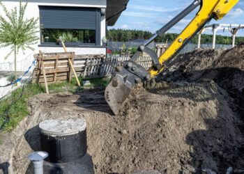 Using an excavator to bury a 10 m3 concrete septic tank located in the garden next to the house