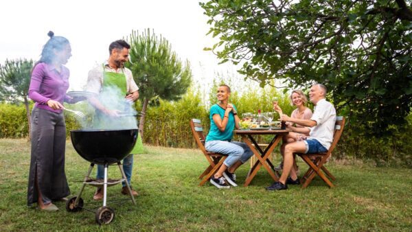 Multiracial couple cooking food on grill for friends Outdoor garden barbecue party Friends laughing and having fun