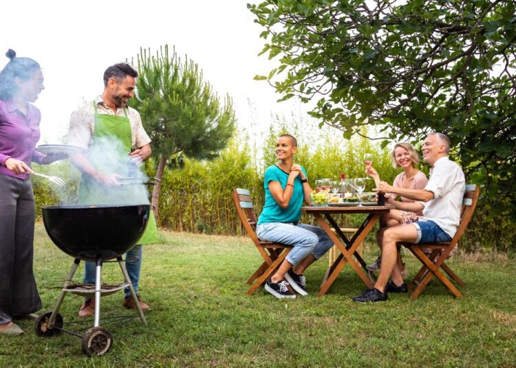 Multiracial couple cooking food on grill for friends Outdoor garden barbecue party Friends laughing and having fun