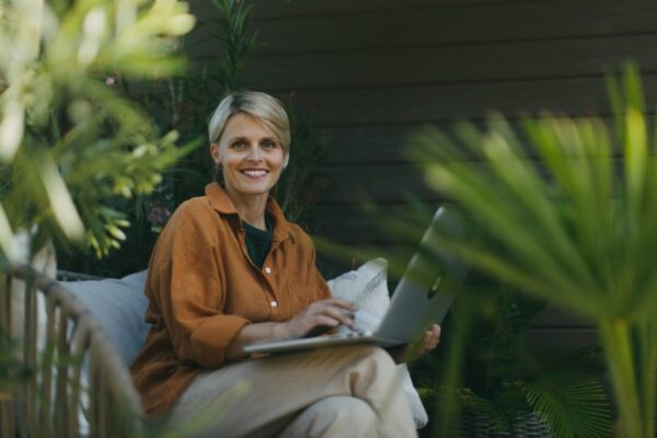 Woman in the garden working on laptop sitting on patio chair Businesswoman working remotely from outdoor home office thinking about new business or creative idea Concept of green outdoor home office