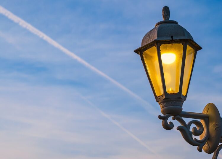 Electric lamp in retro style on a wooden pole The lamp glows against the background of the sky with clouds during sunset Idea for holiday background or postcard copy space for text