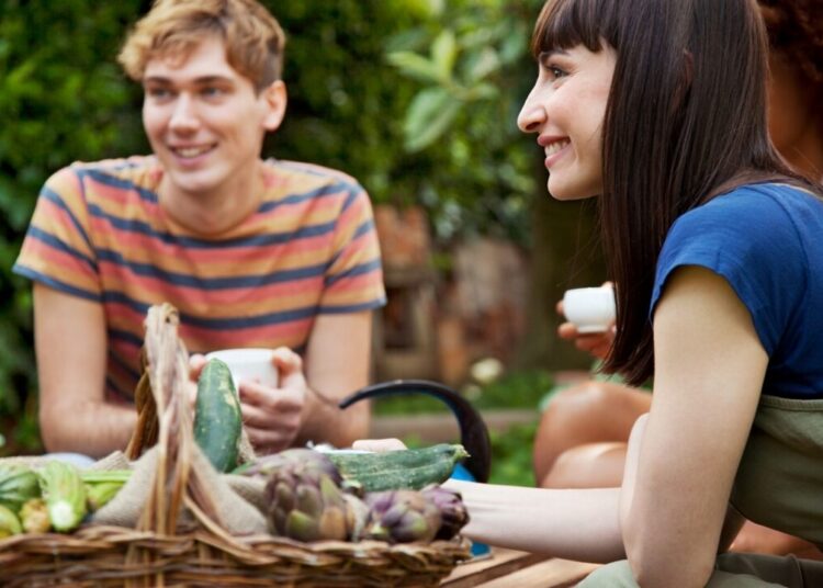 Friends sitting in garden with basket of fresh vegetables