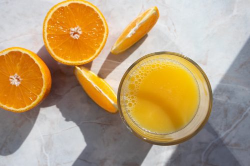 Glass of fresh orange juice and cut oranges on light table
